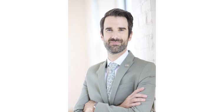 Dr. Tyler Staples leans against brick wall with arms crossed.